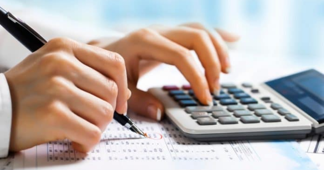 Profesional realizando un cálculo en una calculadora y tomando notas con un lapicero.