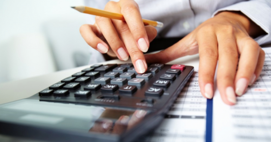 Manos de una mujer usando una calculadora y sosteniendo un lápiz sobre documentos financieros.