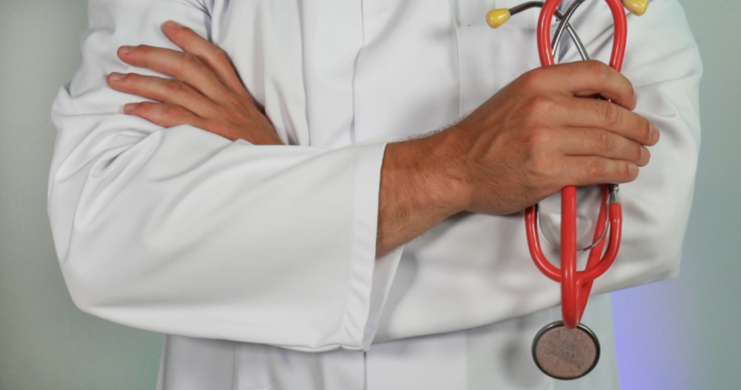 Primer plano de un profesional médico con bata blanca sosteniendo un estetoscopio rojo con los brazos cruzados