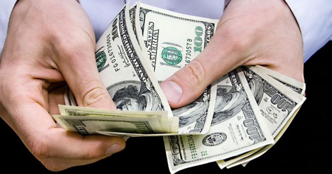 Una persona mostrando varios billetes de dólares.