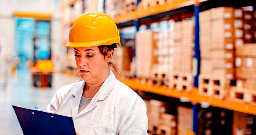Una auditora financiera revisa el stock físico en un almacén logístico utilizando una tableta digital.
